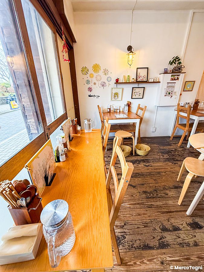 Interno del ristorante vegano Marugoto ad Asakusa con tavoli in legno e una vetrata affacciata sulla strada.
