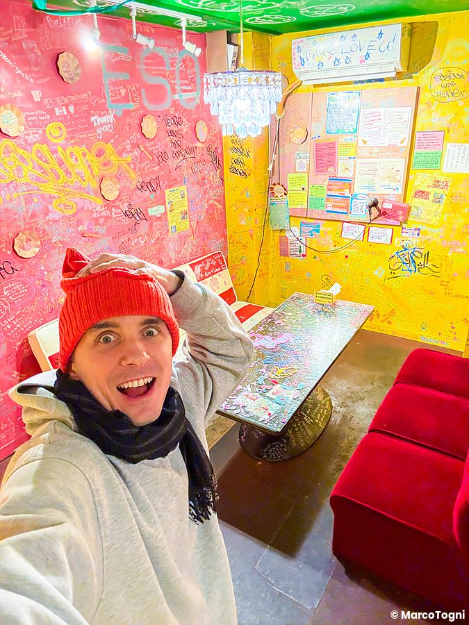 Marco Togni con berretto rosso scatta un selfie all'interno del ristorante OKO ad Osaka, caratterizzato da pareti piene di...