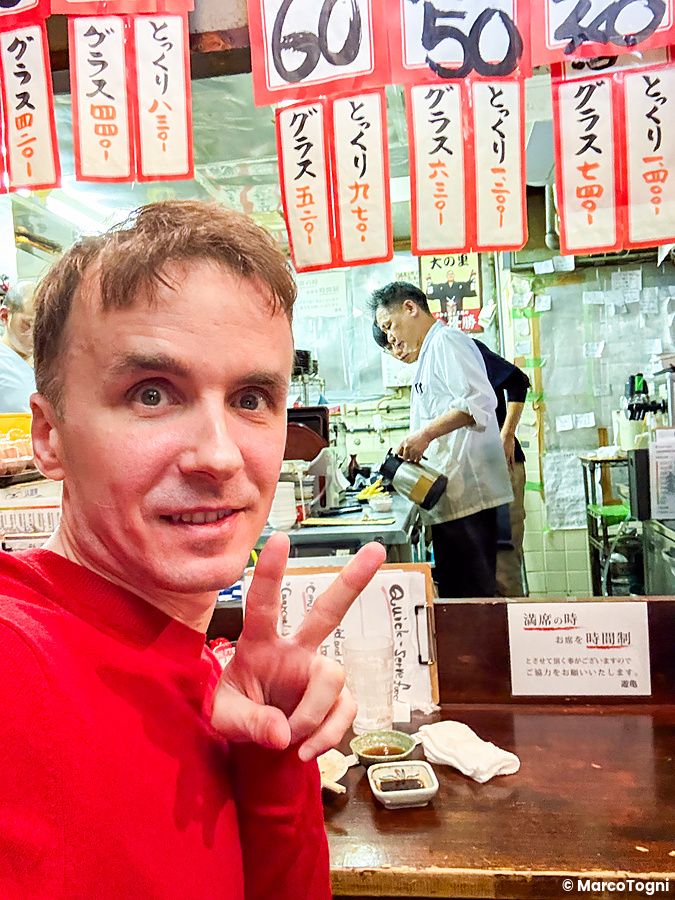 Marco Togni fa il segno di vittoria in un selfie all'interno di Gion Yuki a Kyoto, con personale che lavora dietro il banc...