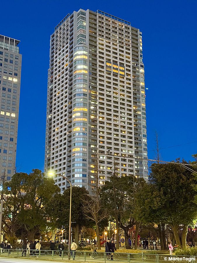 Un imponente grattacielo residenziale svetta sopra un parco nel quartiere di Kinshicho, Tokyo, durante l'ora blu.