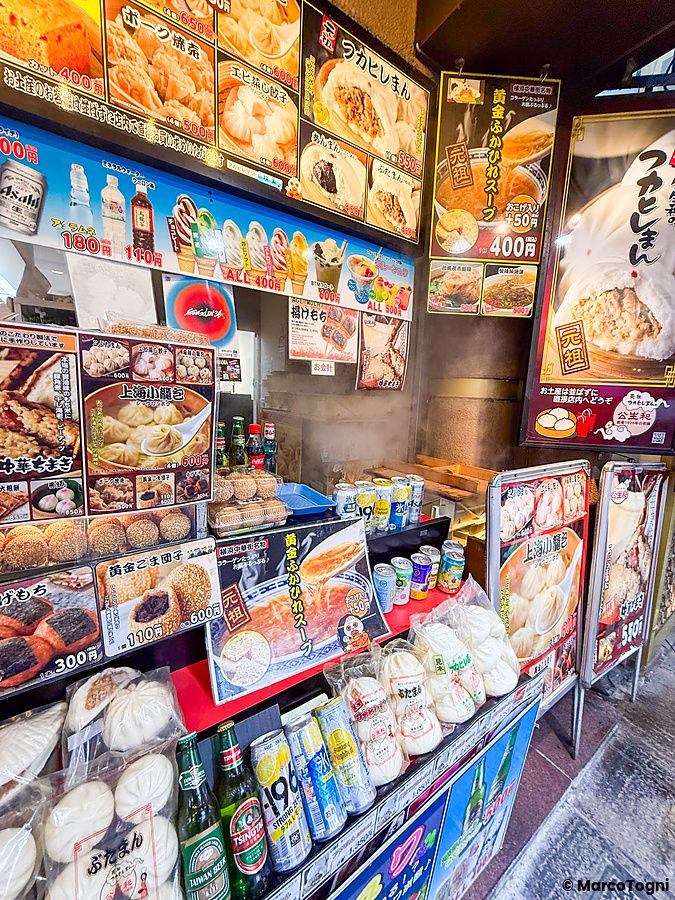 Vetrina del negozio Koseiwa a Chinatown Yokohama, ricca di insegne con foto di dim sum, baozi e varie bevande in vendita.