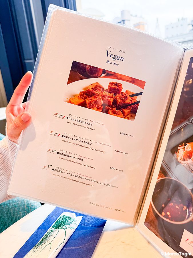 Una mano tiene aperto il menu del ristorante Lotus Palace di Fukuoka che mostra le opzioni della sezione vegana.