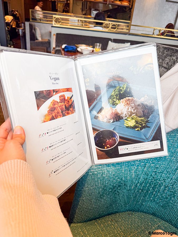 Una mano tiene aperto il menu del ristorante Lotus Palace di Fukuoka che mostra le opzioni di piatti vegani.