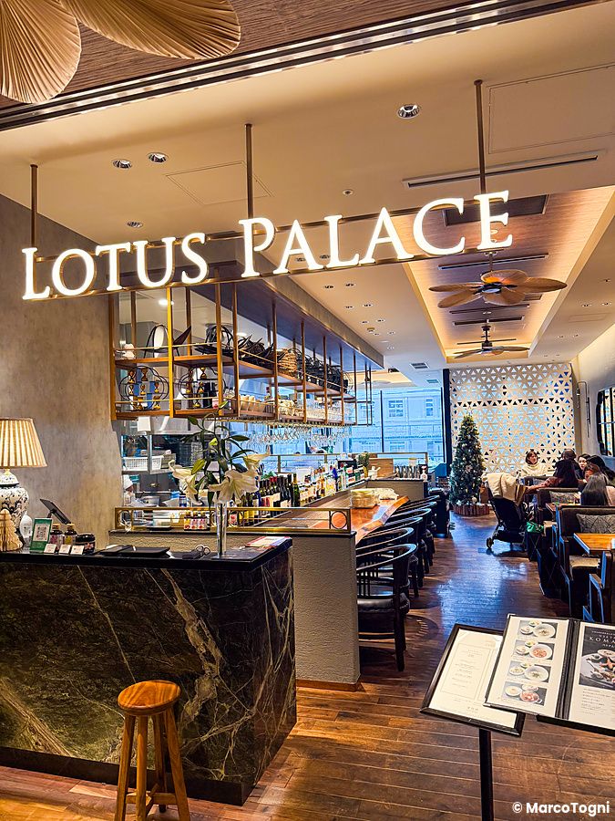 L'interno del ristorante Lotus Palace a Fukuoka con insegna luminosa, bancone in marmo e sala da pranzo con persone.