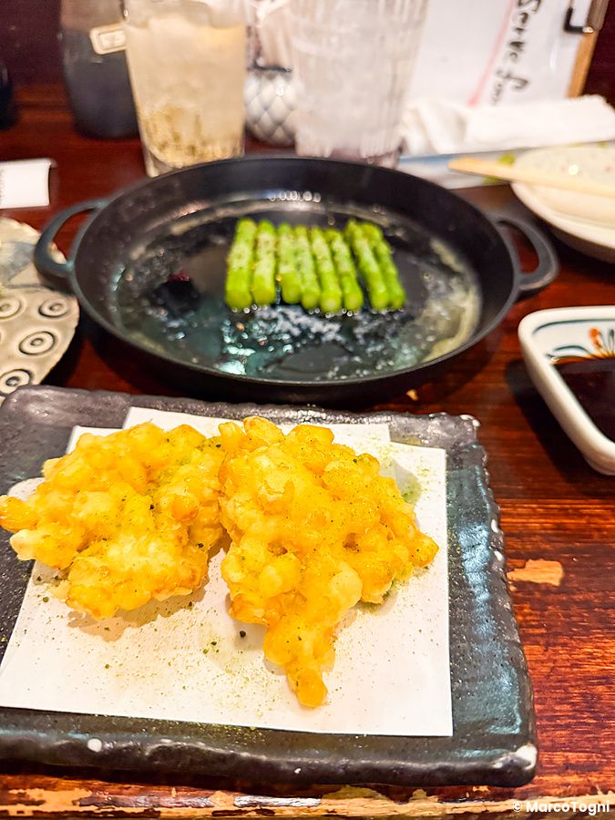 Mais fritto servito su un piattino nero all'interno dell'izakaya Gion Yuki a Kyoto, con asparagi cotti sullo sfondo.