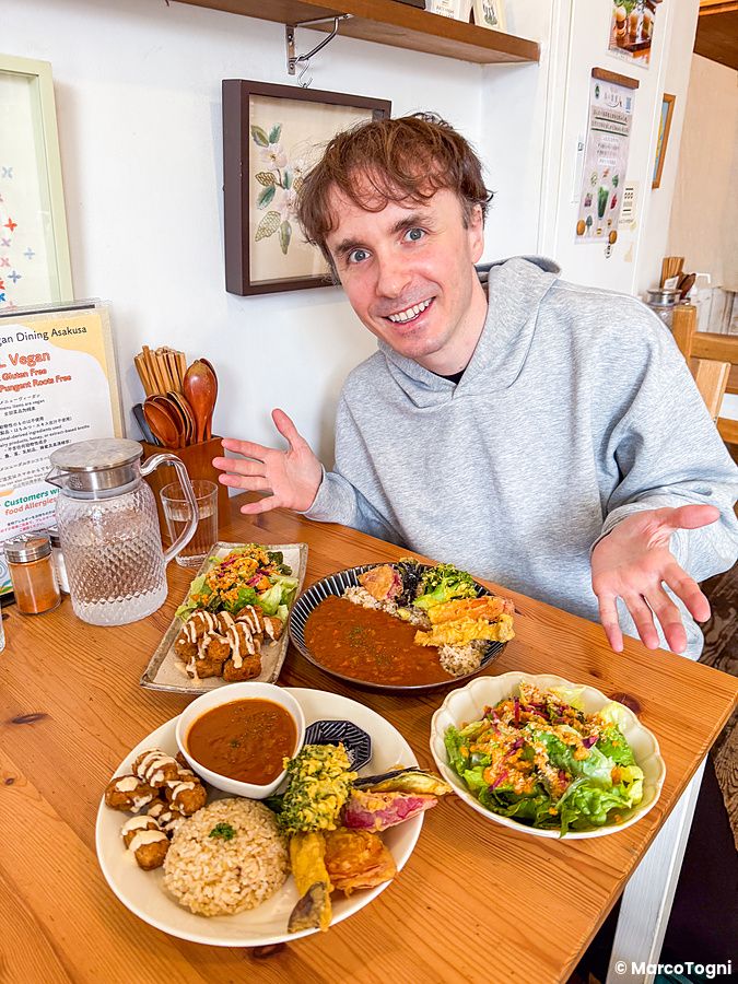 Marco Togni siede a un tavolo di Marugoto Vegan Dining ad Asakusa con piatti di curry, insalata, falafel e altro.