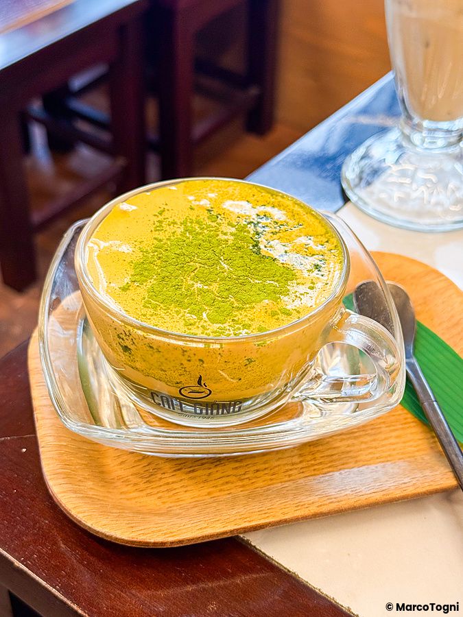 Matcha all'uovo, variante del caffè all'uovo, in una tazza di vetro trasparente su un vassoio di legno a Café Giang.