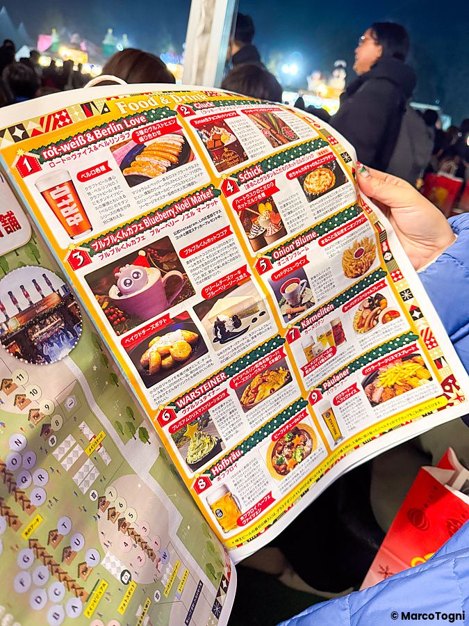 Una mano sostiene un volantino colorato con il menu del Tokyo Christmas Market presso il Meiji Jingu Gaien.