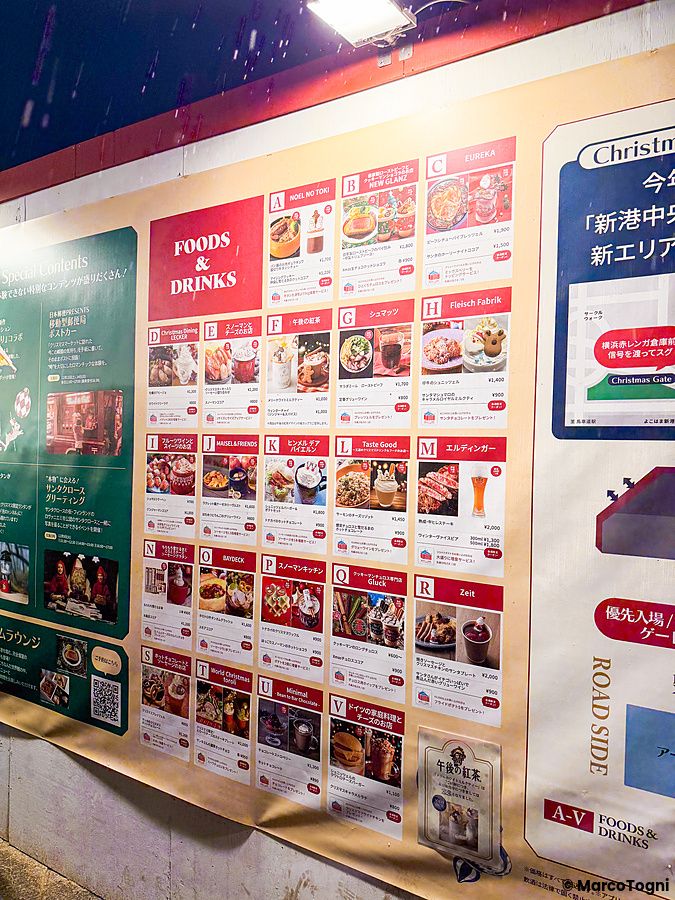 Un pannello informativo con menu illustrati di cibi e bevande presso lo Yokohama Red Brick Christmas Market.