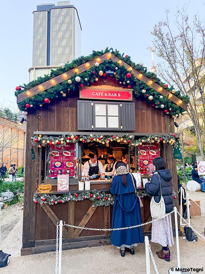 Una casetta in legno decorata per Natale presso il mercato di Azabudai Hills con persone che ordinano al bancone.