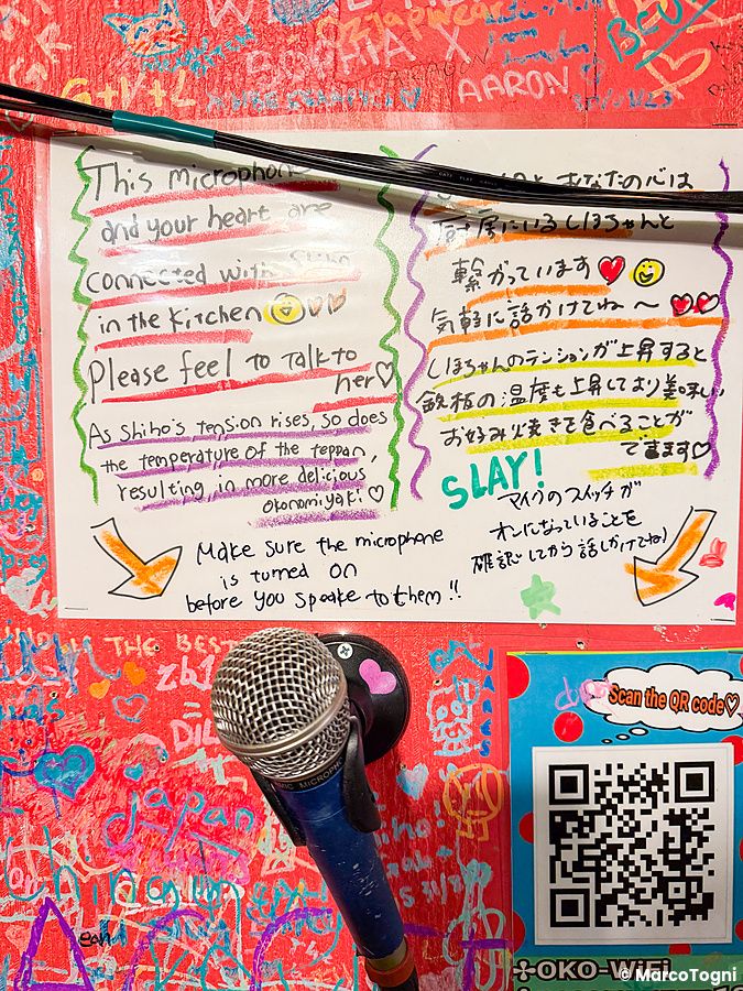 Dettaglio di una parete colorata nel ristorante OKO a Osaka con scritte, un microfono e istruzioni per i clienti.