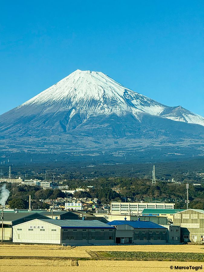 Vista frontale del Monte Fuji innevato e del paesaggio circostante ripresa dall'interno di uno shinkansen.