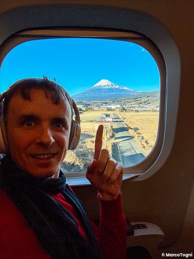 Marco Togni con cuffie a bordo di uno shinkansen N700 Supreme guarda verso la vista del Monte Fuji dallo shinkansen.