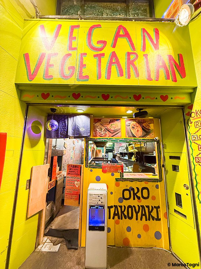 L'ingresso colorato del ristorante OKO ad Osaka, con scritte dipinte a mano sulla facciata gialla e una persona al lavoro.