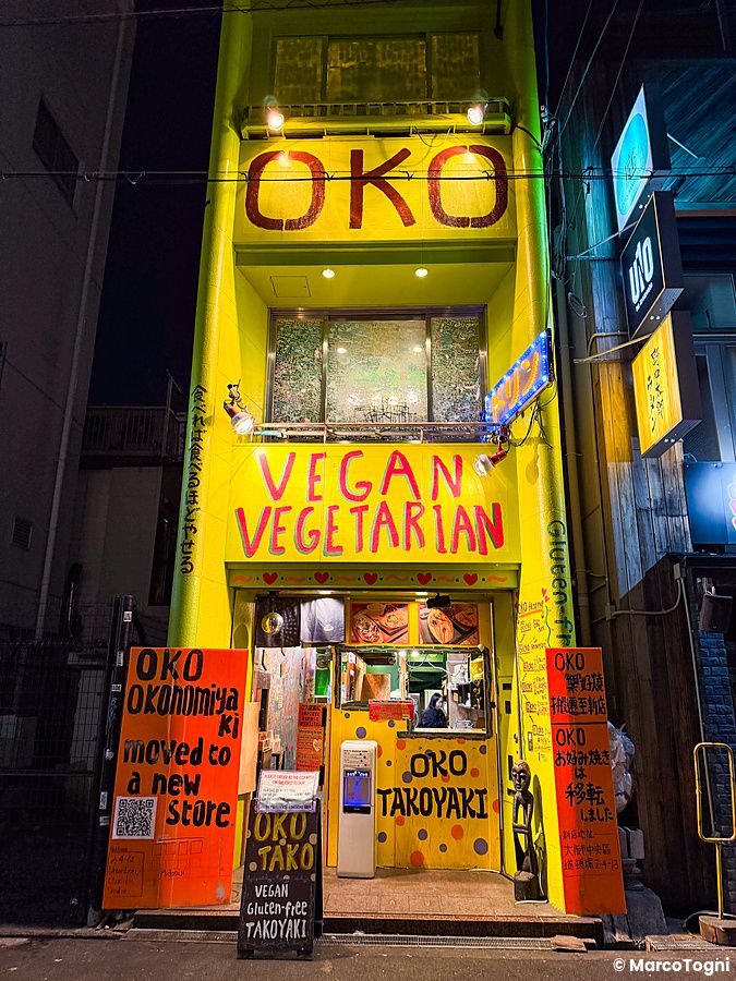 La facciata gialla e vibrante del ristorante OKO ad Osaka con scritte sui muri e un bancone d'ingresso visibile.