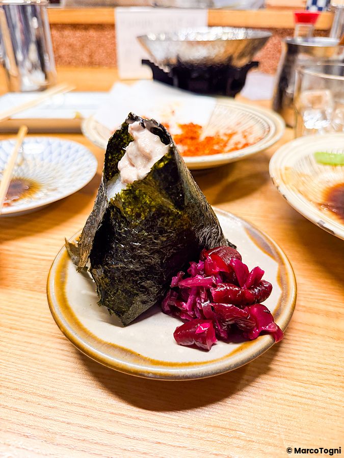 Un onigiri ripieno al Hatonoyu servito su un piattino con sottaceti rossi accanto ad altri piatti consumati.