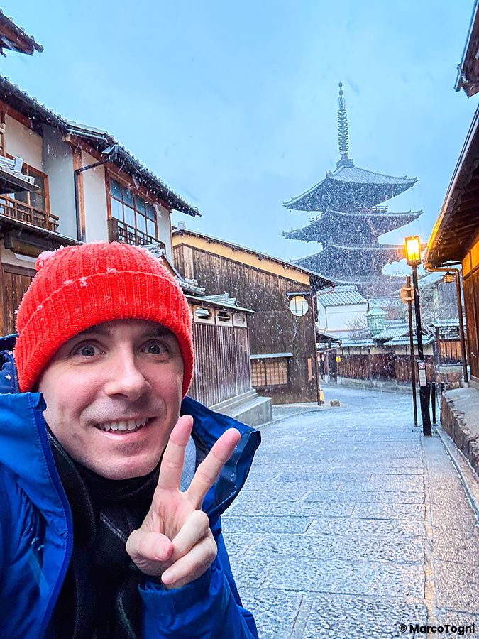 Marco Togni con berretto rosso scatta un selfie davanti alla Pagoda Yasaka a Kyoto durante una nevicata invernale.