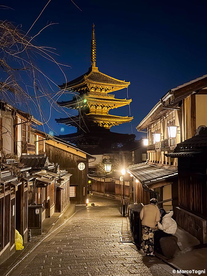 La pagoda Yasaka a a Kyoto domina la strada in salita circondata da edifici tradizionali, con due persone in primo piano.
