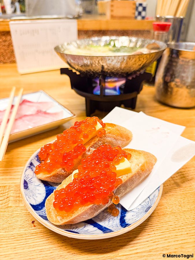 Due fette di pane con ikura e una fetta di burro servite su un piatto decorato all'izakaya Hatonoyu a Tokyo.