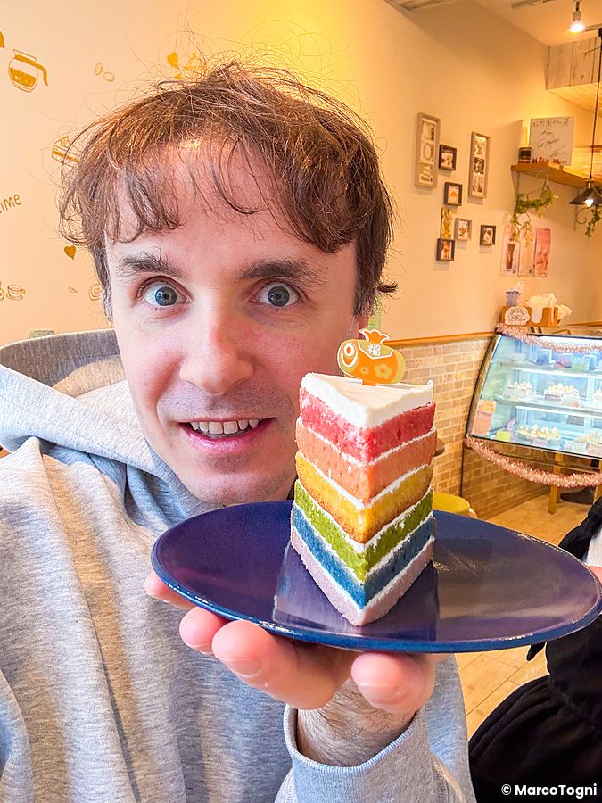Marco Togni tiene in mano un piatto blu con una rainbow cake presso il caffè Shochikuen ad Asakusa.