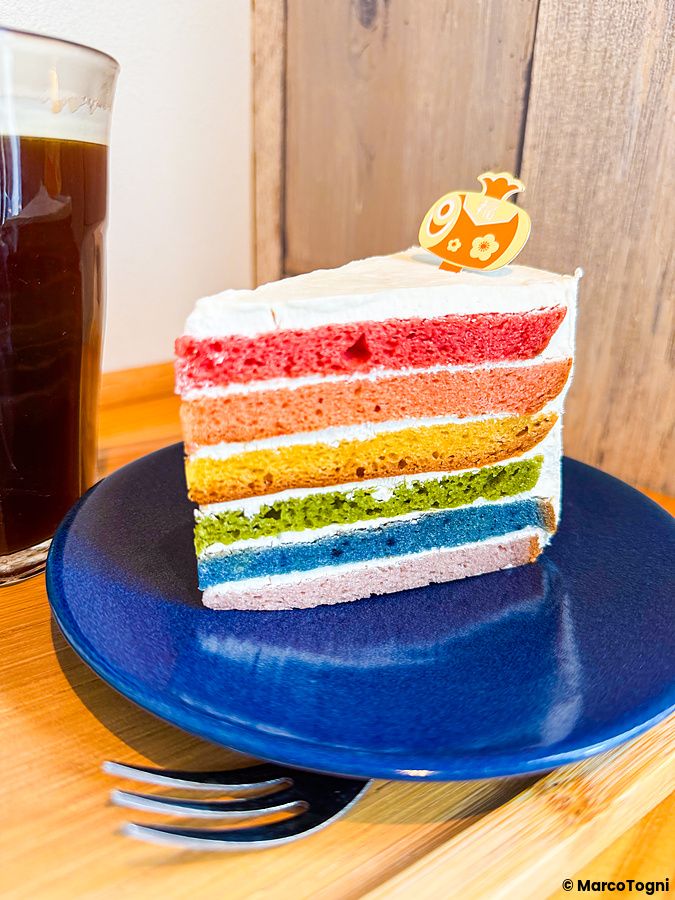 Una fetta di rainbow cake con strati colorati su un piatto blu, servita al caffè Shochikuen ad Asakusa.