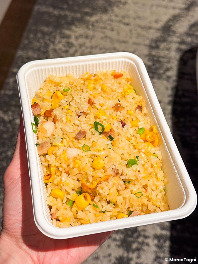 Una mano tiene una vaschetta di plastica bianca contenente riso saltato, d'asporto a Wangfujing.