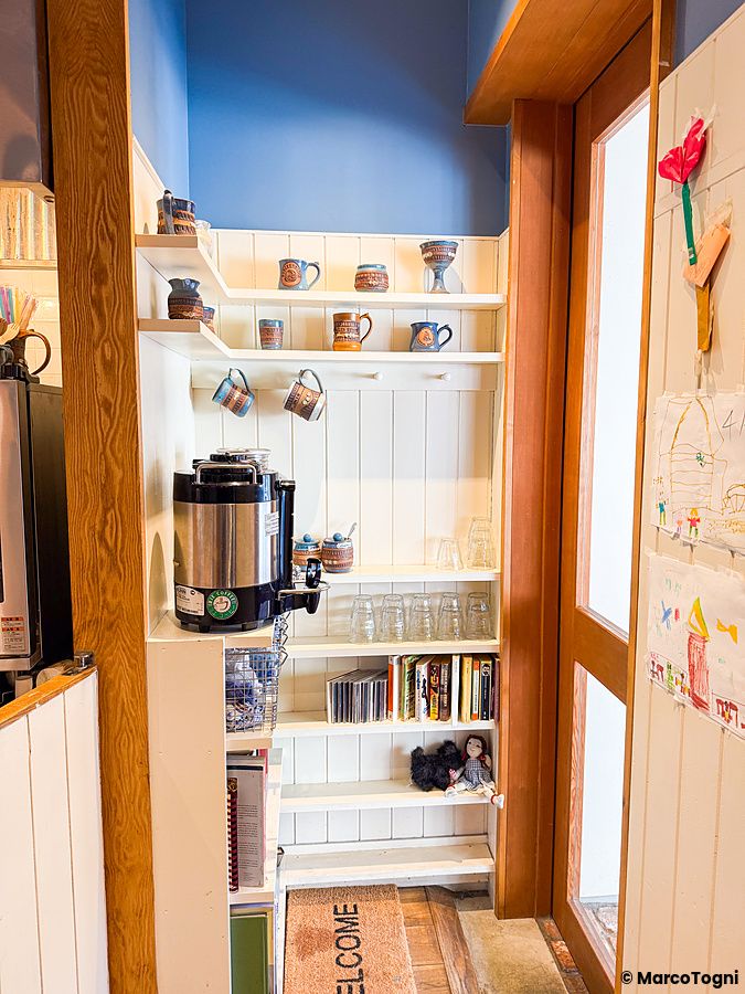 Una scaffalatura bianca in legno con tazze e bicchieri all'interno del caffè RoJean a Tokyo.