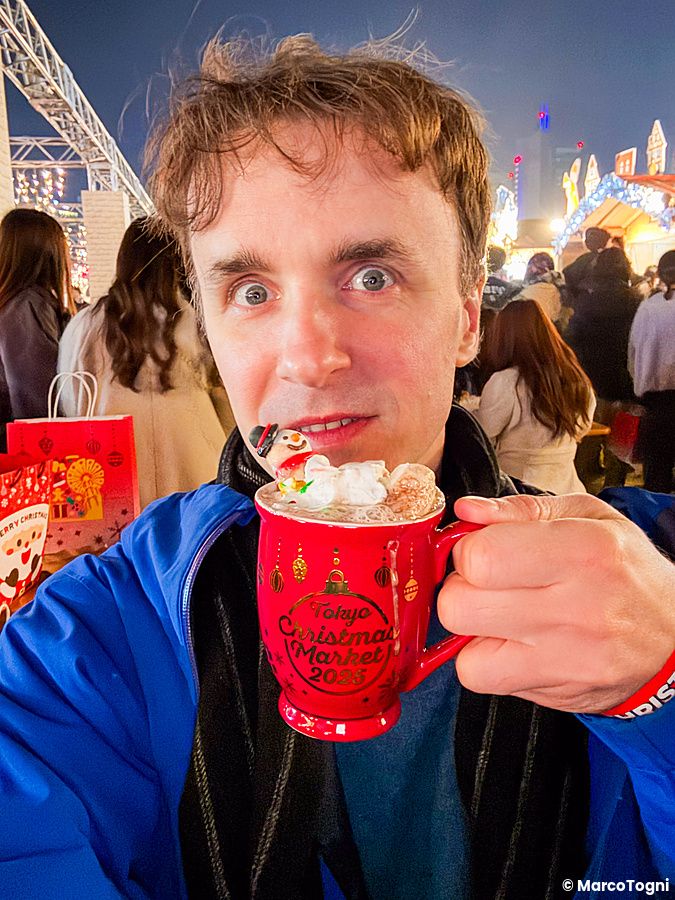 Marco Togni tiene una tazza rossa del Tokyo Christmas Market con un marshmallow a forma di pupazzo di neve davanti al viso.