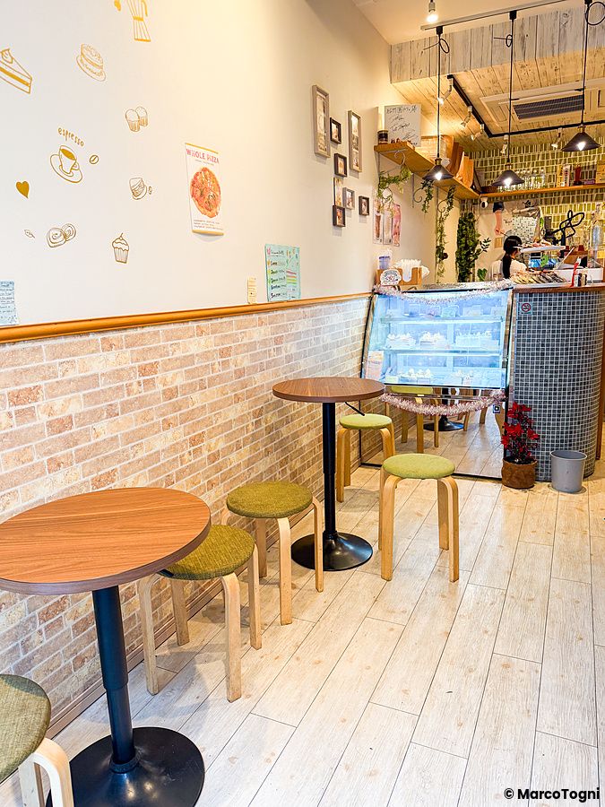 Interno a Shochikuen ad Asakusa con tavoli in legno, sgabelli verdi e una vetrina per dolci presso il bancone.
