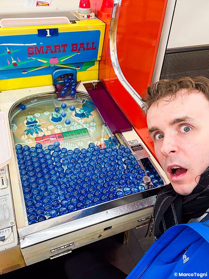 Marco Togni con espressione sorpresa accanto a un dispositivo di gioco Smart Ball all'interno di Smartball New Star a Osaka.