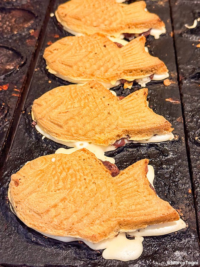 Taiyaki a forma di pesce in fase di cottura su una piastra metallica scura presso Hakata Hiiragi Taiyaki.