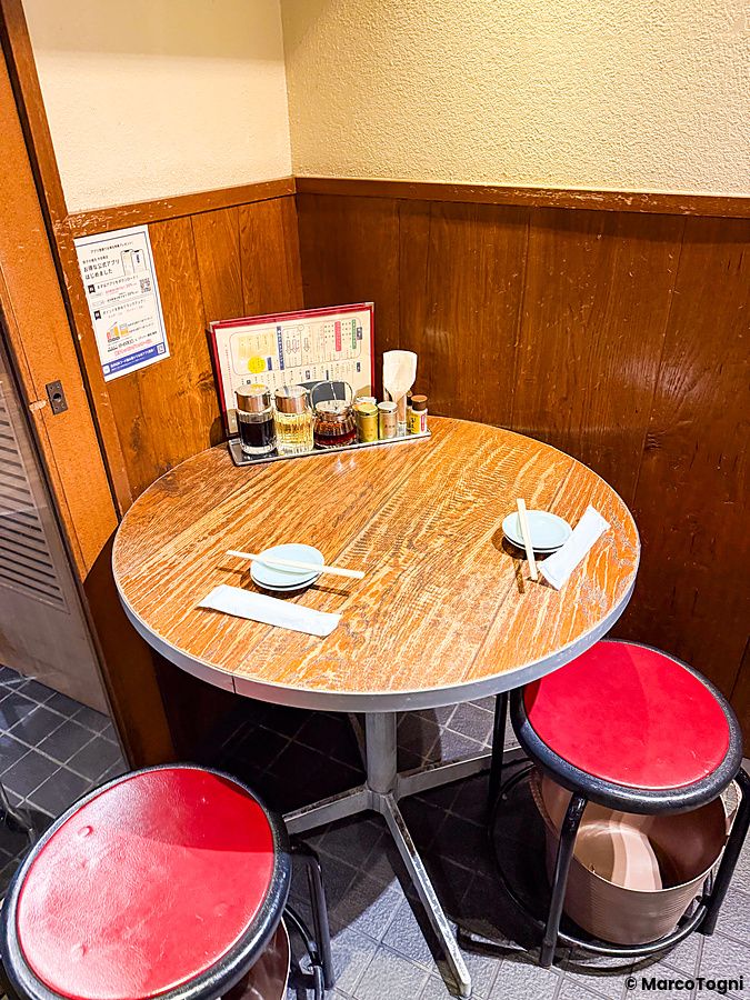 Tavolo rotondo con due sgabelli rossi all'interno del ristorante Gyoza no Fukuho.