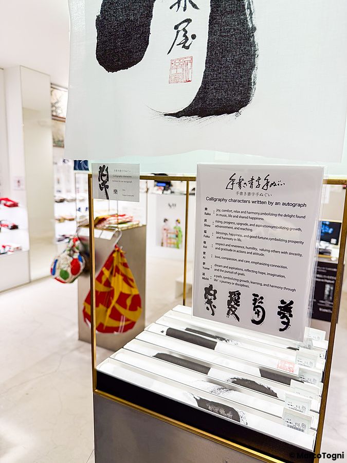 Espositore con tenugui e cartello informativo sulla calligrafia nel negozio Eirakuya a Kyoto.