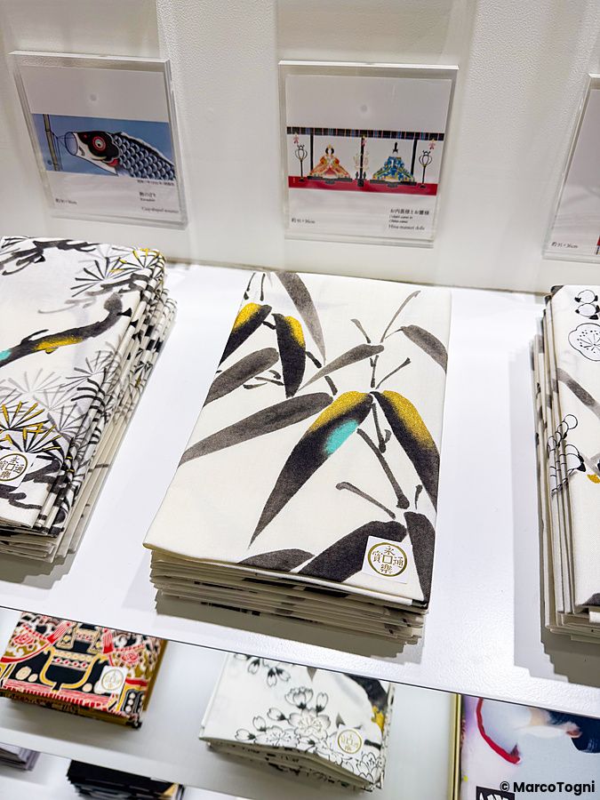 Tenugui ripiegati con stampe artistiche in vendita sugli scaffali del negozio Eirakuya a Kyoto.