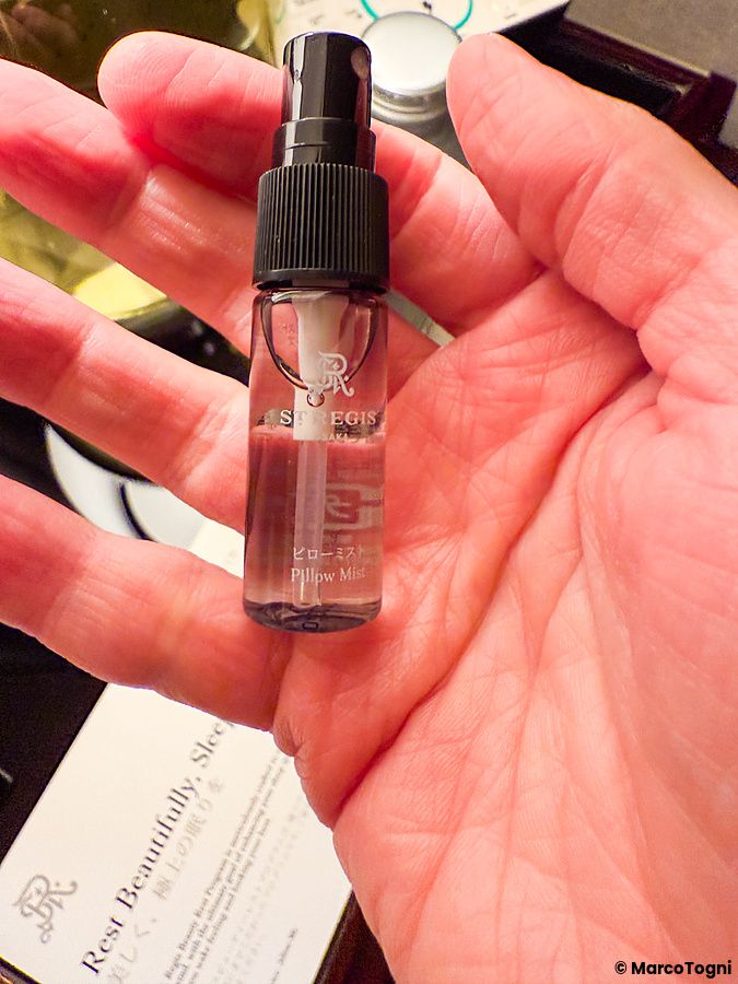 Una mano aperta tiene una boccetta di spray per cuscini brandizzata durante il turndown service a The St. Regis Osaka.