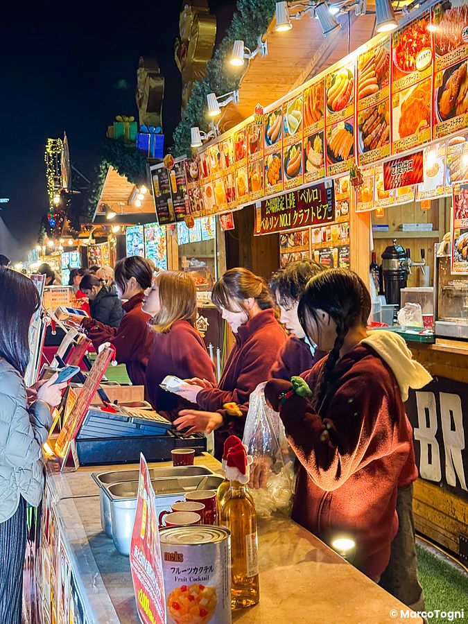 Diverse persone lavorano in una bancarella alimentare presso il Tokyo Christmas Market al Meiji Jingu Gaien di sera.