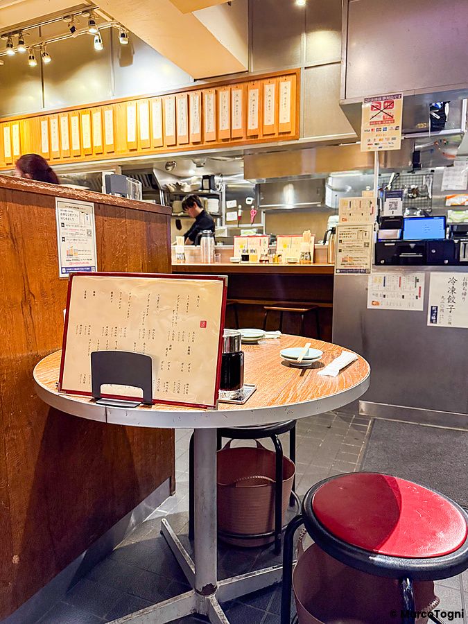 L'interno del ristorante Gyoza no Fukuho a Tokyo con un tavolino rotondo in primo piano e il bancone cucina sullo sfondo.