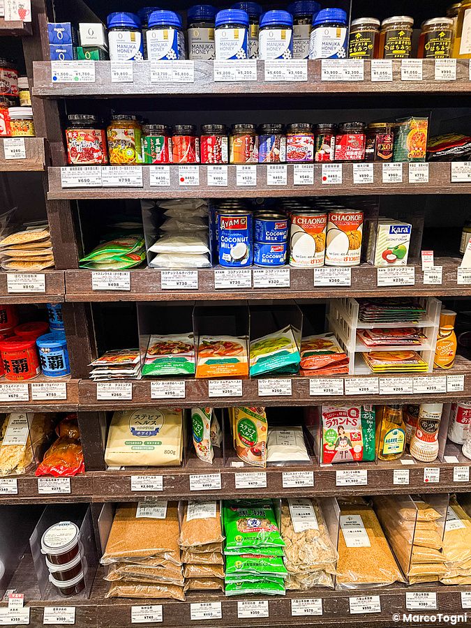 Scaffali pieni di prodotti alimentari e ingredienti in vendita presso il negozio Tomizawa Shoten a Machida.