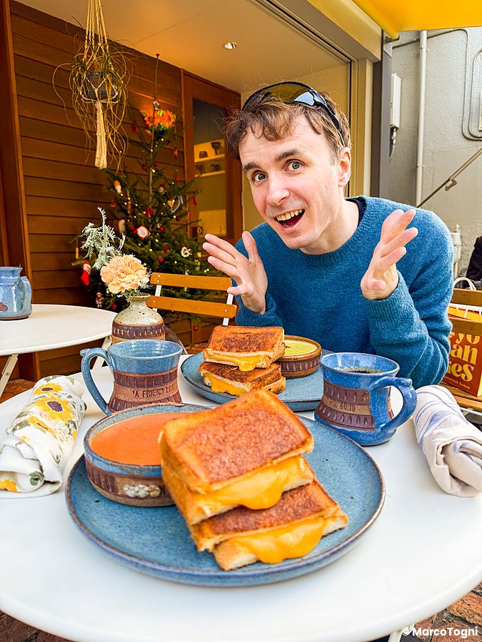 Marco Togni sorridente siede a un tavolo con tost con formaggio a RoJean, un caffè specializzato in colazioni a Tokyo.