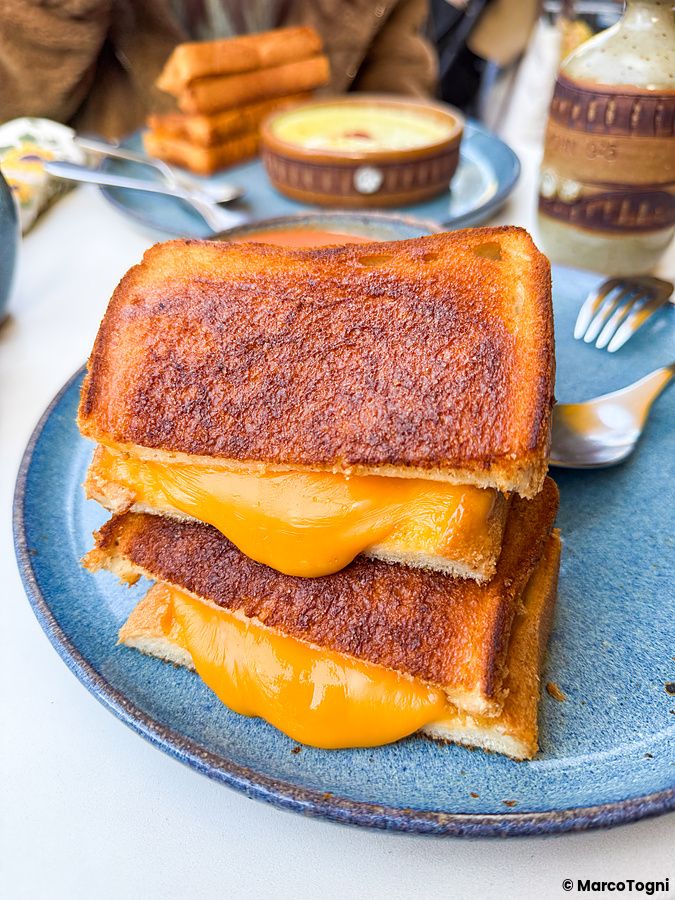 Un tost con formaggio fuso su un piatto blu in primo piano nel caffè RoJean a Tokyo.