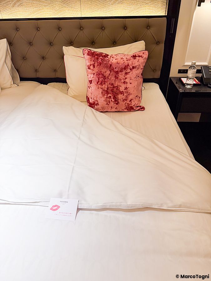 Un letto rifatto con turndown service a Fauchon Hotel Kyoto, con un biglietto di cortesia bianco sul piumino.