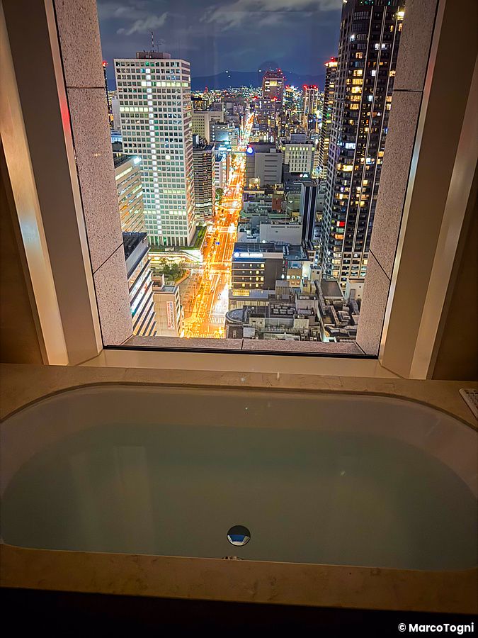 Una vasca da bagno si affaccia su un panorama notturno di grattacieli e strade illuminate vista dalla stanza a The St. Reg...
