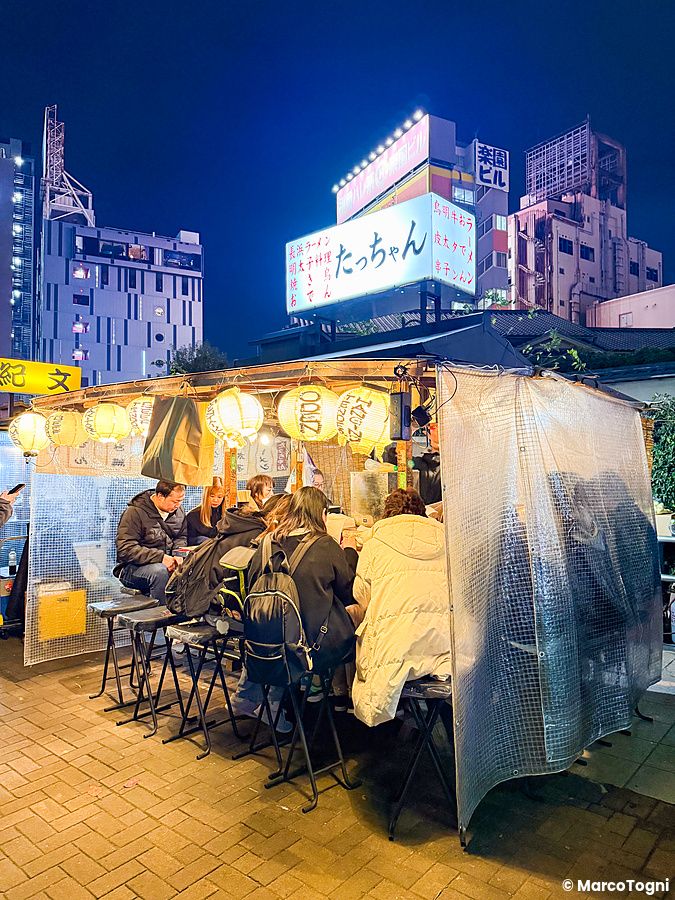 Una bancarella yatai a Fukuoka illuminata di sera con diverse persone sedute al bancone per mangiare.