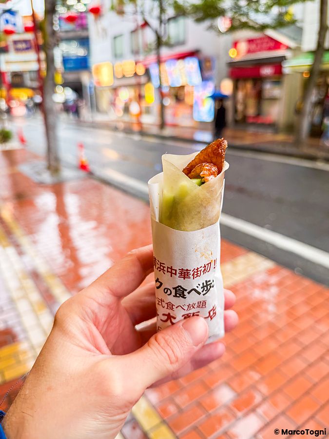 Una mano tiene un'anatra alla pechinese da asporto in carta al Chukagai Daihanten nella Chinatown di Yokohama.