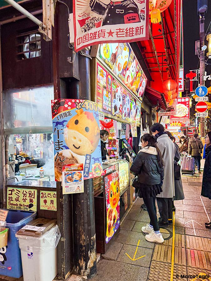 Persone in fila davanti a una bancarella di street food nella Chinatown di Yokohama durante una serata illuminata.