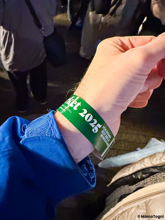 Un braccialetto verde con la scritta "2025" al polso di una persona al Yokohama Red Brick Christmas Market.