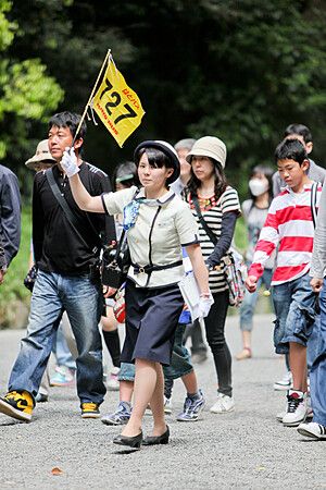 Guida turistica giapponese con gruppo su un sentiero alberato.