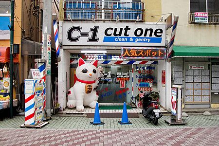 Un maneki neko gigante giappone posizionato all'ingresso di un parrucchiere in Giappone.