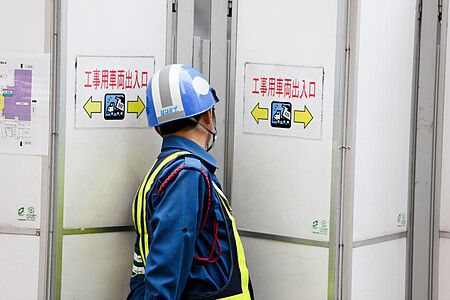 Un operaio giapponese barriere a in Giappone indossa un elmetto e una divisa blu mentre sorveglia un passaggio di cantiere.