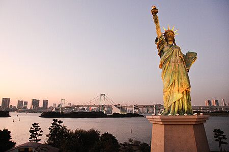 La Statua della Libertà ad Odaiba in Giappone con il Rainbow Bridge visibile sullo sfondo durante il tramonto.